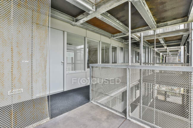 Enge Halle mit Tür und Fenstern gegen rostige Metallzäune unter Dach mit Balken am Tag — Stockfoto