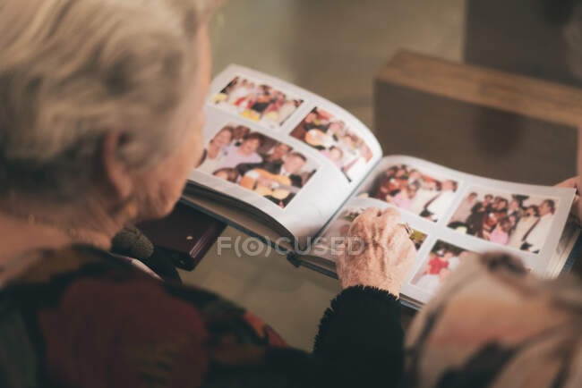 De arriba recorte femenino sentado en sillón y demostrando fotos familiares de álbum de fotos a otra persona - foto de stock