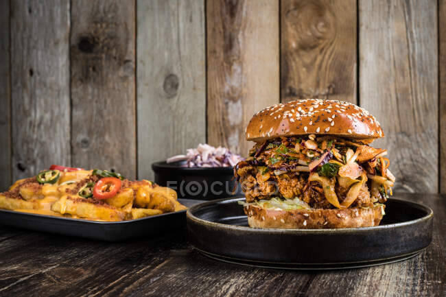 Аппетитный бургер с мясом на гриле помещен рядом с подносом для выпечки с картошкой фри с перцем и миской с салатом на деревянном столе в ресторане — стоковое фото