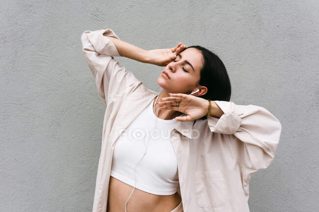 Carefree female dancer listening to music in earphones and dancing with closed eyes while enjoying songs on background of gray wall in city — Stock Photo