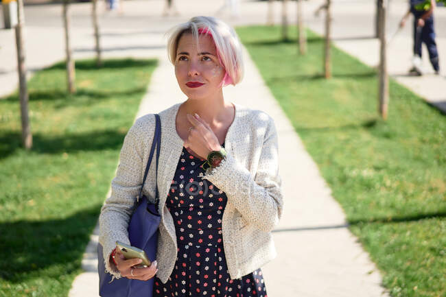 Mulher alternativa alegre com cabelo tingido em pé na rua e navegar na Internet no telefone celular no verão — Fotografia de Stock