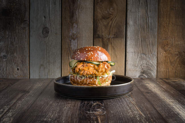 Hambúrguer de frango apetitoso com legumes frescos e molho servido em prato preto na mesa de madeira — Fotografia de Stock