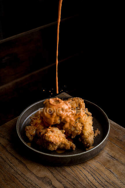 Зверху смачного соусу наливають хрустку курку, розміщену на круглій тарілці на дерев'яному столі в ресторані — стокове фото