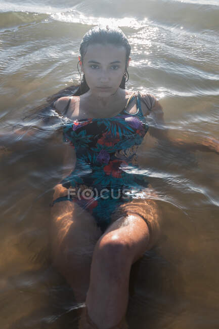 Serena fêmea com cabelo molhado nadando em mar calmo na noite de verão e olhando para a câmera — Fotografia de Stock