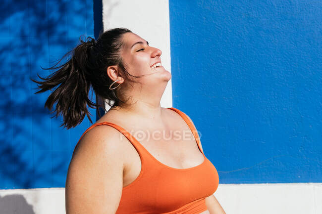 Desportista étnica rechonchuda alegre no desgaste ativo com cabelo voador se divertindo no dia ensolarado — Fotografia de Stock