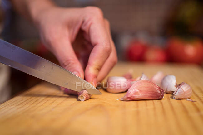 Ernte unkenntlich Frau schneidet frischen Knoblauch mit Messer auf Schneidebrett beim Kochen in der heimischen Küche — Stockfoto