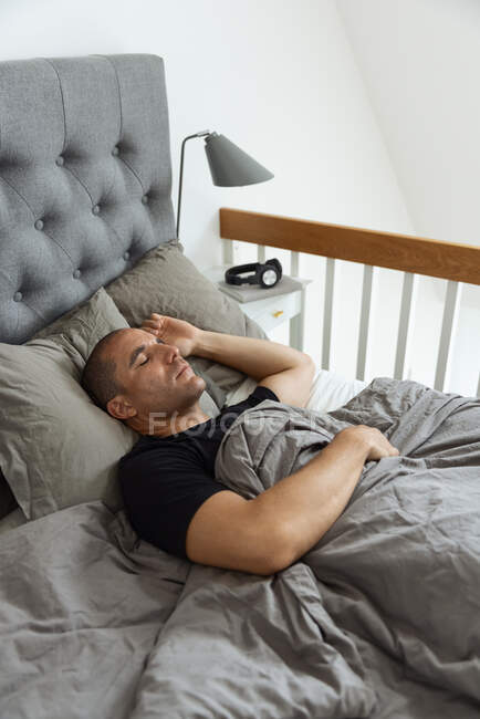 De cima de pacífico macho deitado em cama macia sob cobertor e dormindo de manhã no quarto — Fotografia de Stock