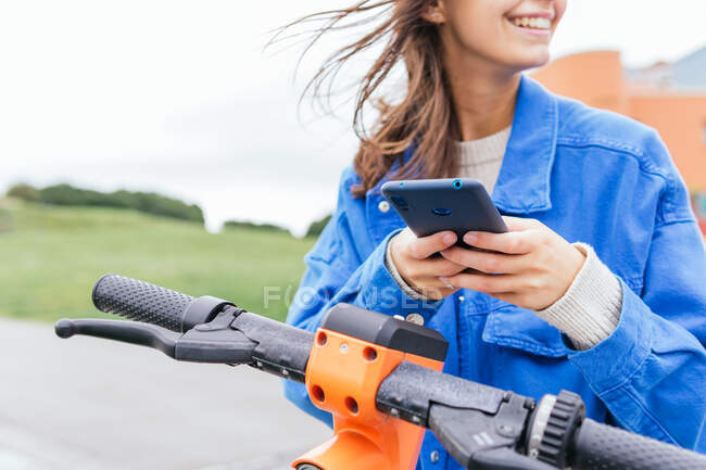 Content female renting parked electric scooter in city and browsing mobile phone — Stock Photo