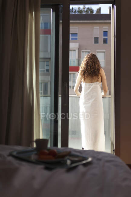 Vista posteriore della donna con i capelli ricci sulla terrazza della sua camera da letto in una giornata di sole con colazione a letto — Foto stock