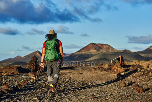 Caminhante anônimo com mochila andando no caminho seco no vale perto de colinas no dia nublado de verão em Fuerteventura, Espanha — Fotografia de Stock