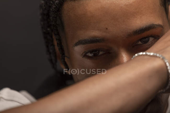 Headshot de jovem afro-americano sério masculino com cabelo trançado e pulseira no pulso olhando para a câmera pensativa — Fotografia de Stock