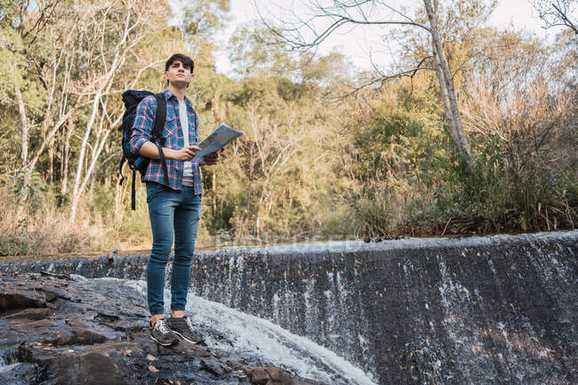 Baixo ângulo do caminhante masculino com mochila navegando com mapa de papel enquanto está em pé na floresta e olhando para longe — Fotografia de Stock