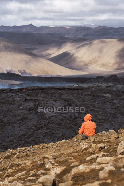 Rückansicht eines nicht wiederzuerkennenden Touristen, der den Fagradalsfjall bewundert, in dem sich Lava und Rauch zwischen Bergen unter wolkenverhangenem Himmel in Island ausbreiten — Stockfoto