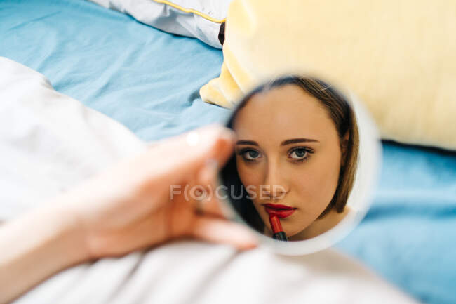 Female reflecting in mirror in bathroom and applying facial cream during skin care routine in morning — Stock Photo