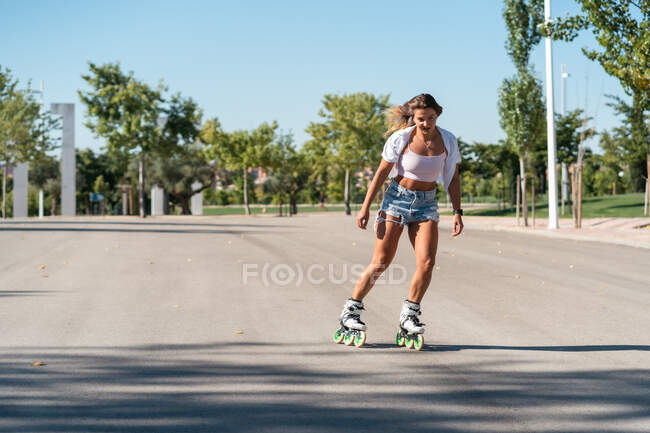 Vista laterale della femmina in forma in pattini mostrando acrobazia su strada in città in estate — Foto stock