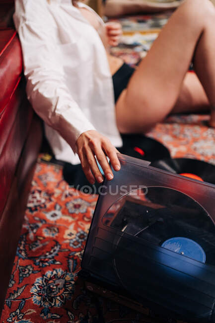Side view of crop unrecognizable female in white shirt and lingerie listening to song from vintage vinyl record player at home — Stock Photo