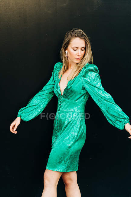 Vista lateral da fêmea serena em vestido verde na moda em pé sobre fundo marrom e olhando para longe — Fotografia de Stock