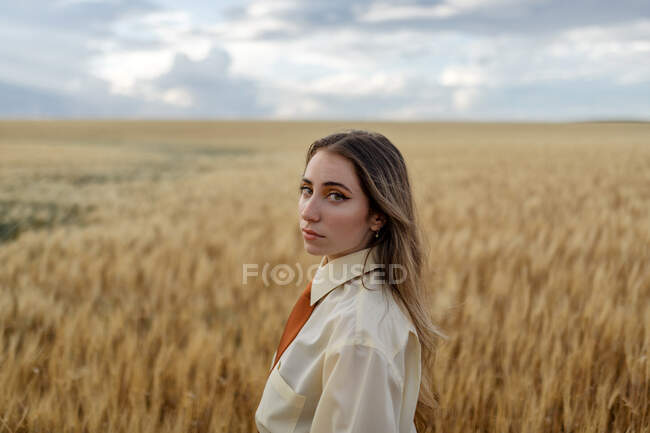 Вид сбоку на молодую заботливую женщину в формальной одежде с галстуком, смотрящую на камеру среди шпионов в сельской местности — стоковое фото
