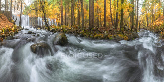 Scenic view of mount with cascades and river with foamy water fluids on stones between autumn trees in Lozoya, Madrid, Spain. — Stock Photo