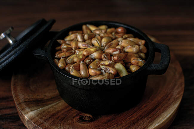 Високий кут нагромадження зерна зернових у чорній каструлі з кришкою, розміщеною на дерев'яній дошці на столі на кухні — стокове фото
