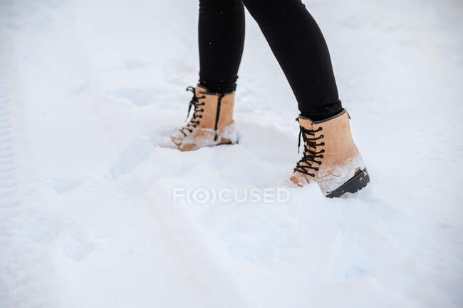 Colheita fêmea irreconhecível em botas quentes em pé no chão nevado no dia de inverno — Fotografia de Stock