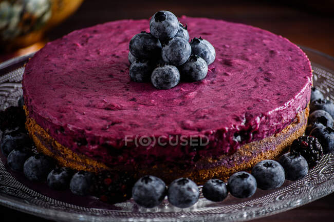 Смачний чорничний мус з фіолетовим кремом, прикрашений свіжими ягодами, поданими на скляній підставці на темному столі — стокове фото
