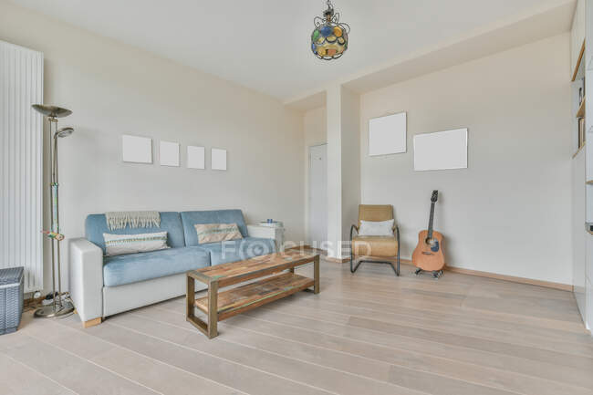 Design de interiores de estilo minimalista moderno de espaçosa sala de estar leve com sofá confortável e poltrona colocado perto da guitarra acústica contra a parede bege com imagens mockup — Fotografia de Stock