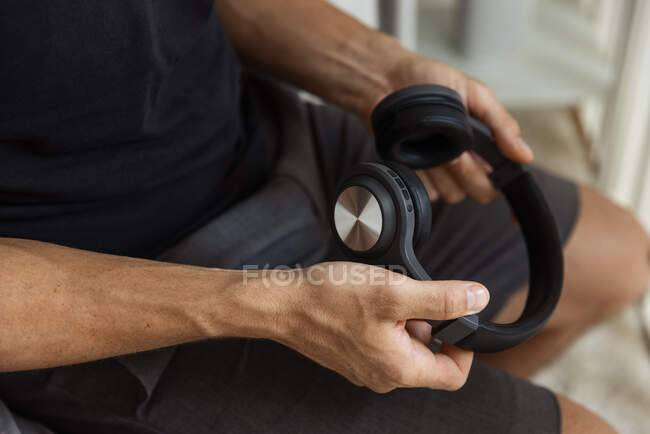 Desde arriba de la cosecha macho anónimo sentado con auriculares inalámbricos modernos en casa - foto de stock