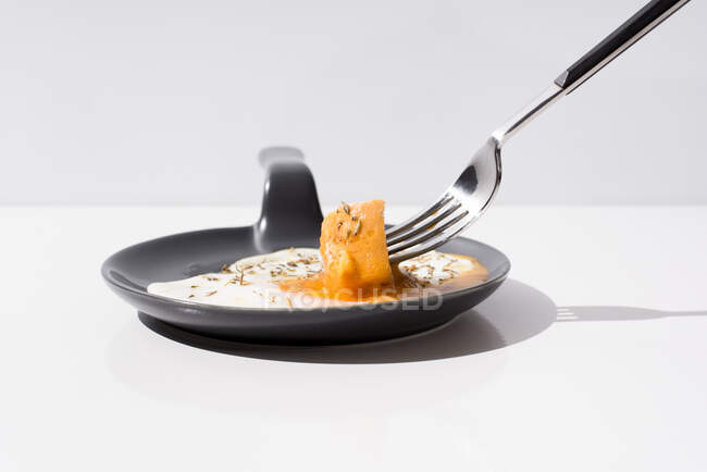 Garfo de metal com pedaço de pão fresco mergulhado em gema líquida de ovo frito servido em frigideira no fundo branco — Fotografia de Stock