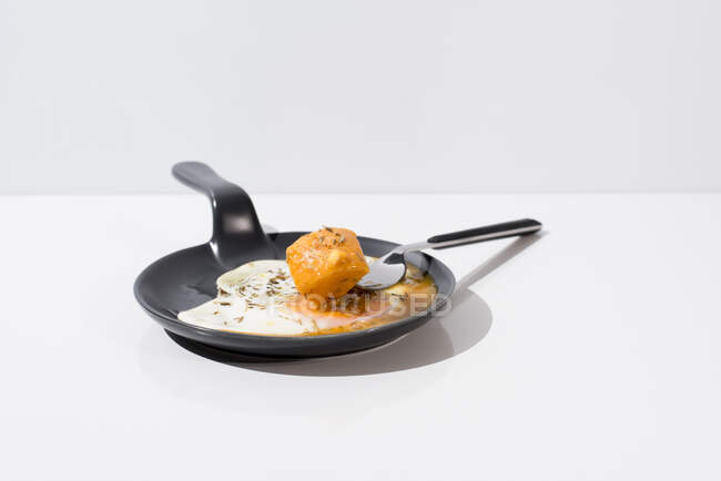 Металлическая вилка со свежим кусочком хлеба, окунутым в жидкий желток жареного яйца, подается на сковороде на белом фоне — стоковое фото