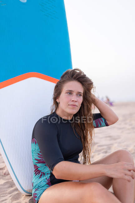 Surferin sitzt im Sommer mit blauem SUP-Board am Sandstrand und schaut weg — Stockfoto
