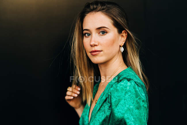 Seitenansicht einer gelassenen Frau im trendigen grünen Kleid, die auf braunem Hintergrund steht und in die Kamera blickt — Stockfoto