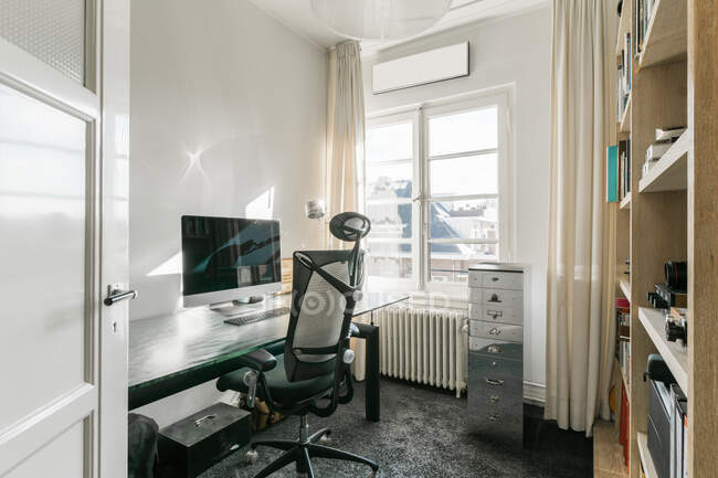 Poltrona confortável colocado perto da mesa com monitor de computador no local de trabalho moderno com prateleiras no apartamento contemporâneo — Fotografia de Stock