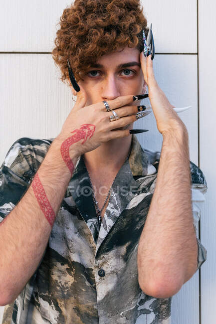 Jeune homme vaniteux en tenue élégante avec de longs ongles debout sur le mur carrelé regardant la caméra — Photo de stock