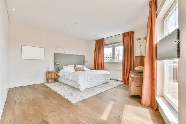 Helles Schlafzimmer mit weißen Wänden und Bett mit großen Fenstern und orangefarbenem Vorhang im modernen Loft-Stil — Stockfoto