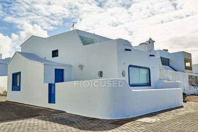 Contemporary house with white walls and blue windows located near pavement against cloudy sky on sunny day in Fuerteventura, Spain — Stock Photo