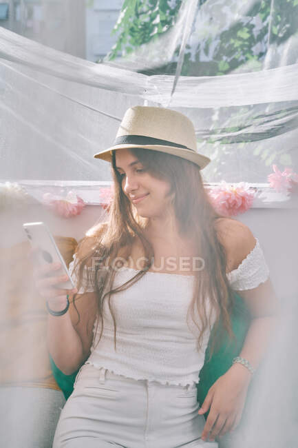 Contenuto femminile seduta sul divano e messaggistica sul telefono cellulare nella giornata di sole in tenda cortile — Foto stock