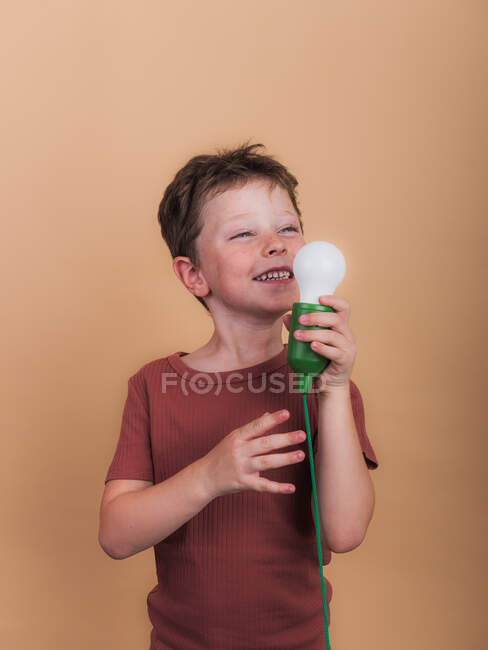 Bambino meditante in t-shirt con lampadina di plastica che rappresenta idea concetto guardando su sfondo beige — Foto stock
