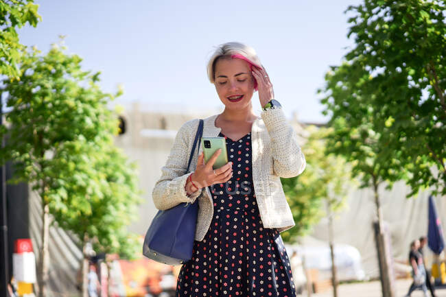 Fröhliche Alternative mit gefärbten Haaren, die im Sommer auf der Straße steht und mit dem Handy im Internet surft — Stockfoto