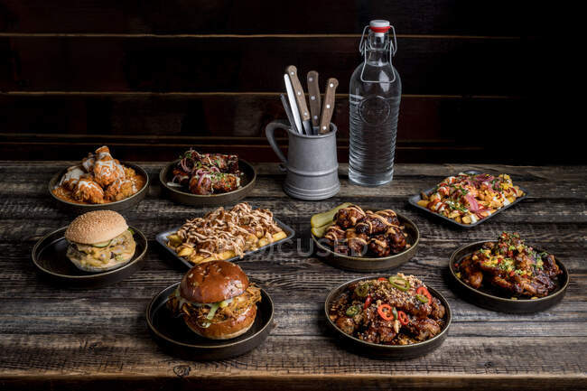 Mesa de madera servida con hamburguesas apetitosas y alas de pollo en restaurante de comida callejera - foto de stock