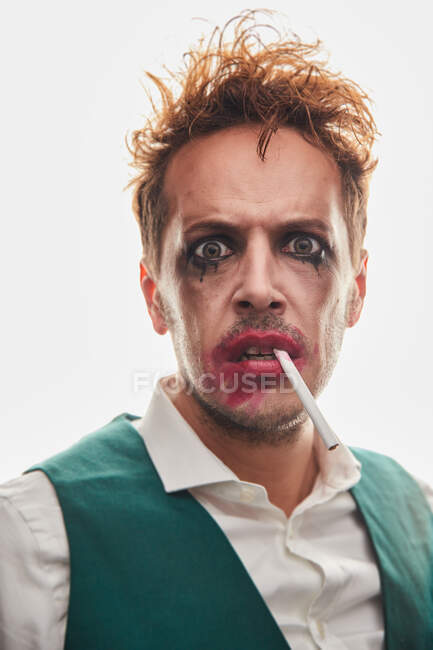 Verblüffter männlicher Schauspieler mit verschmiertem Make-up und Zigarette blickt in die Kamera auf weißem Hintergrund im Studio — Stockfoto