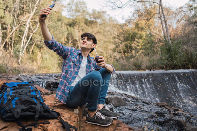 Zufriedener männlicher Wanderer mit Rucksack macht unterwegs Selfie — Stockfoto