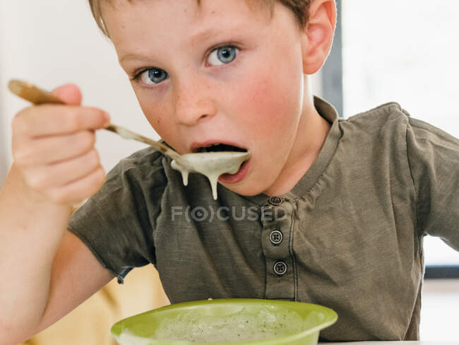 Menino sentado à mesa com tigela de sopa de creme durante o almoço e olhando para longe — Fotografia de Stock