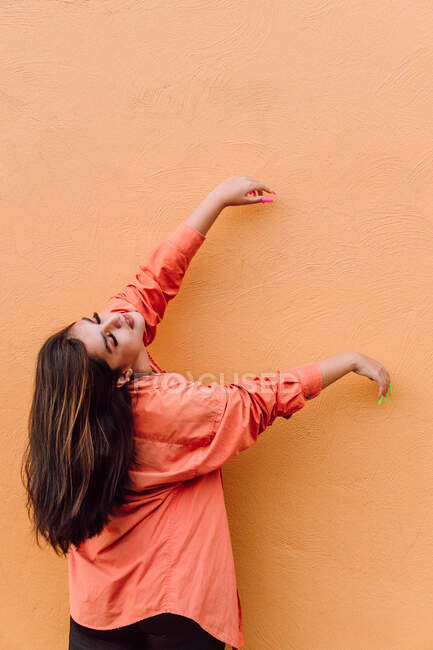 Young woman in modern outfit with bright long manicure raising hands against orange background — Stock Photo