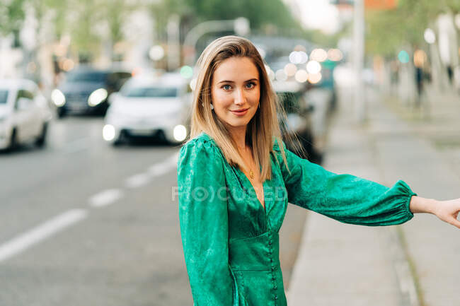 Femme insouciante en robe verte tendance debout dans la rue et regardant la caméra — Photo de stock