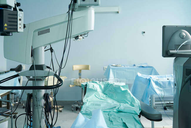 Lit médical avec tissu entre moniteur et microscope chirurgical contre tables et chaise à l'hôpital — Photo de stock