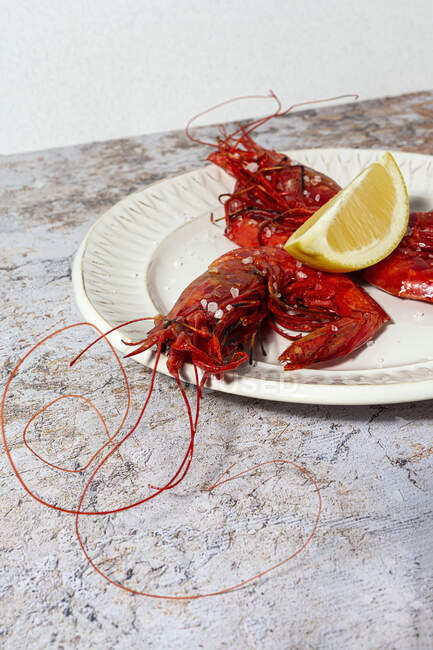 Frutos do mar saborosos de camarões vermelhos cozidos com fatias de limão frescas e sal grosso no fundo branco — Fotografia de Stock