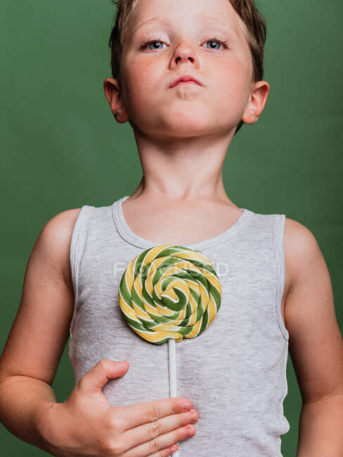 Kid with sweet swirl lollipop towards camera on green background in studio — Stock Photo