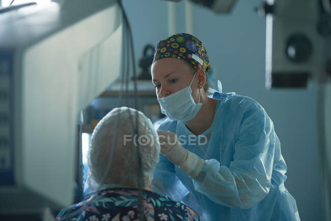 Attentive female surgeon in sterile uniform examining eye of anonymous patient against refractometer in hospital — Stock Photo