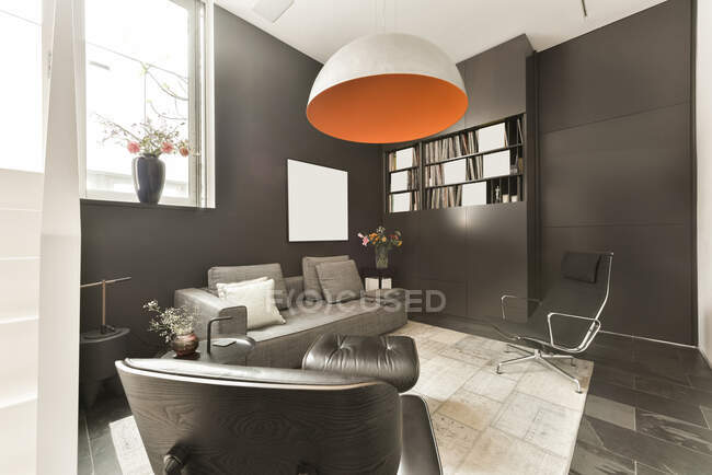 Дизайн інтер'єру вітальні з зручним диваном і шкіряним кріслом в сучасній квартирі з чорними стінами і плиткою підлоги — стокове фото